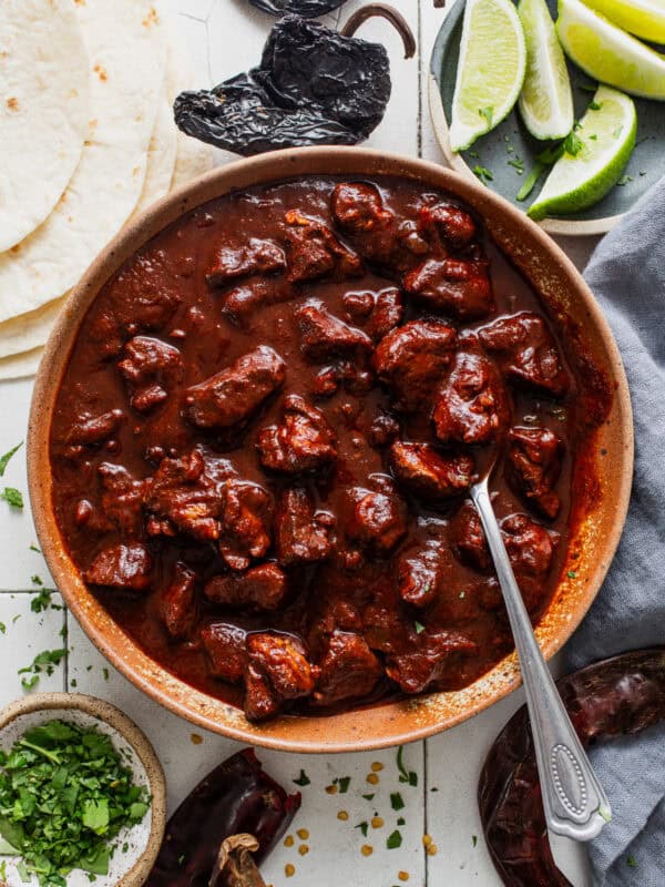Carne adovada in a bowl next to warm tortillas.