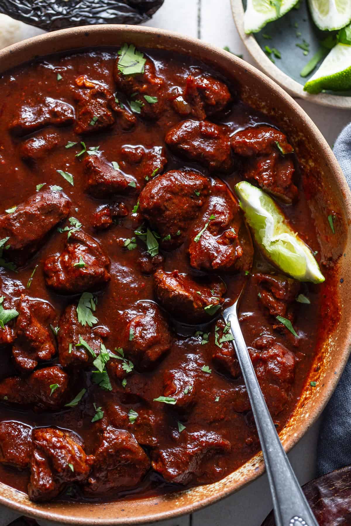 Carne adovada in a bowl with cilantro and a lime.