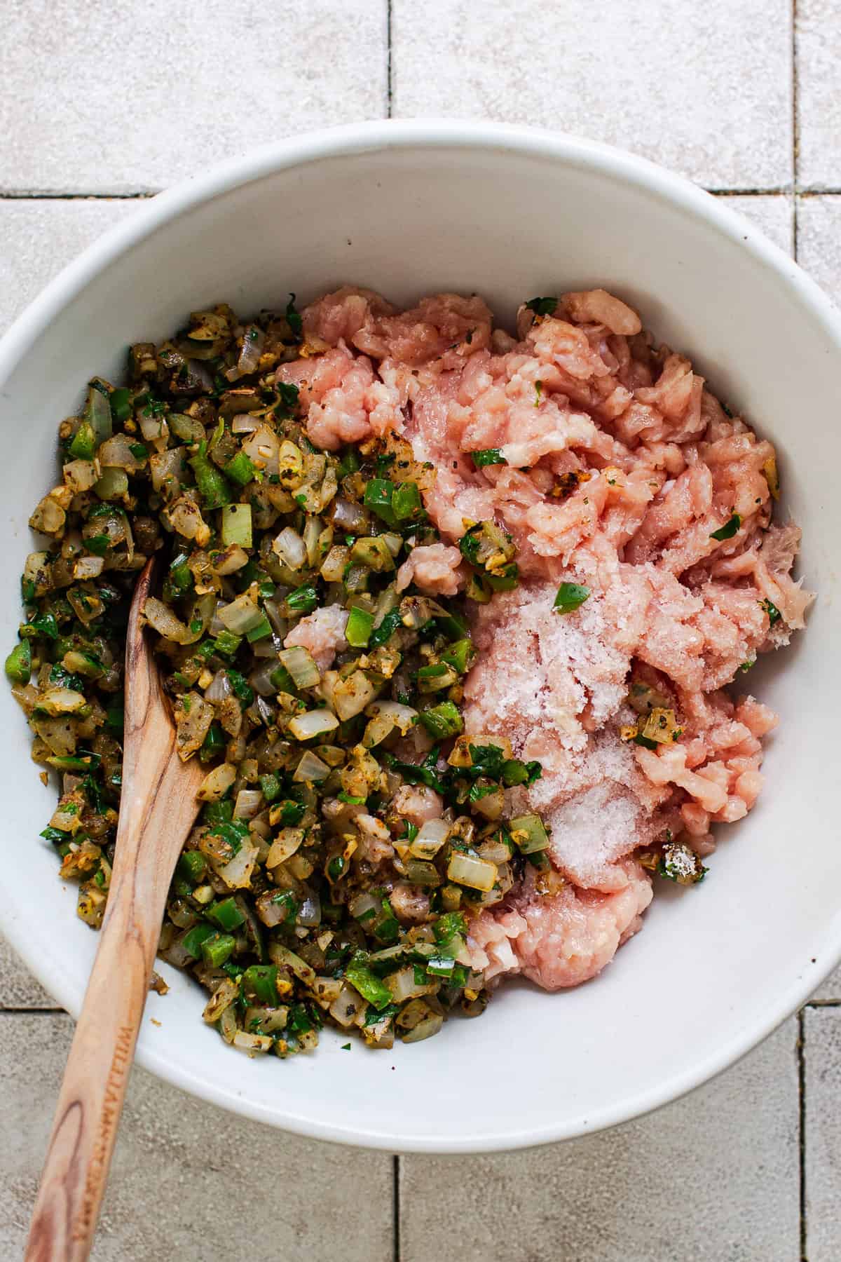 Ground chicken mixed with peppers, onions, seasonings, lime, and salt in a bowl before combining.