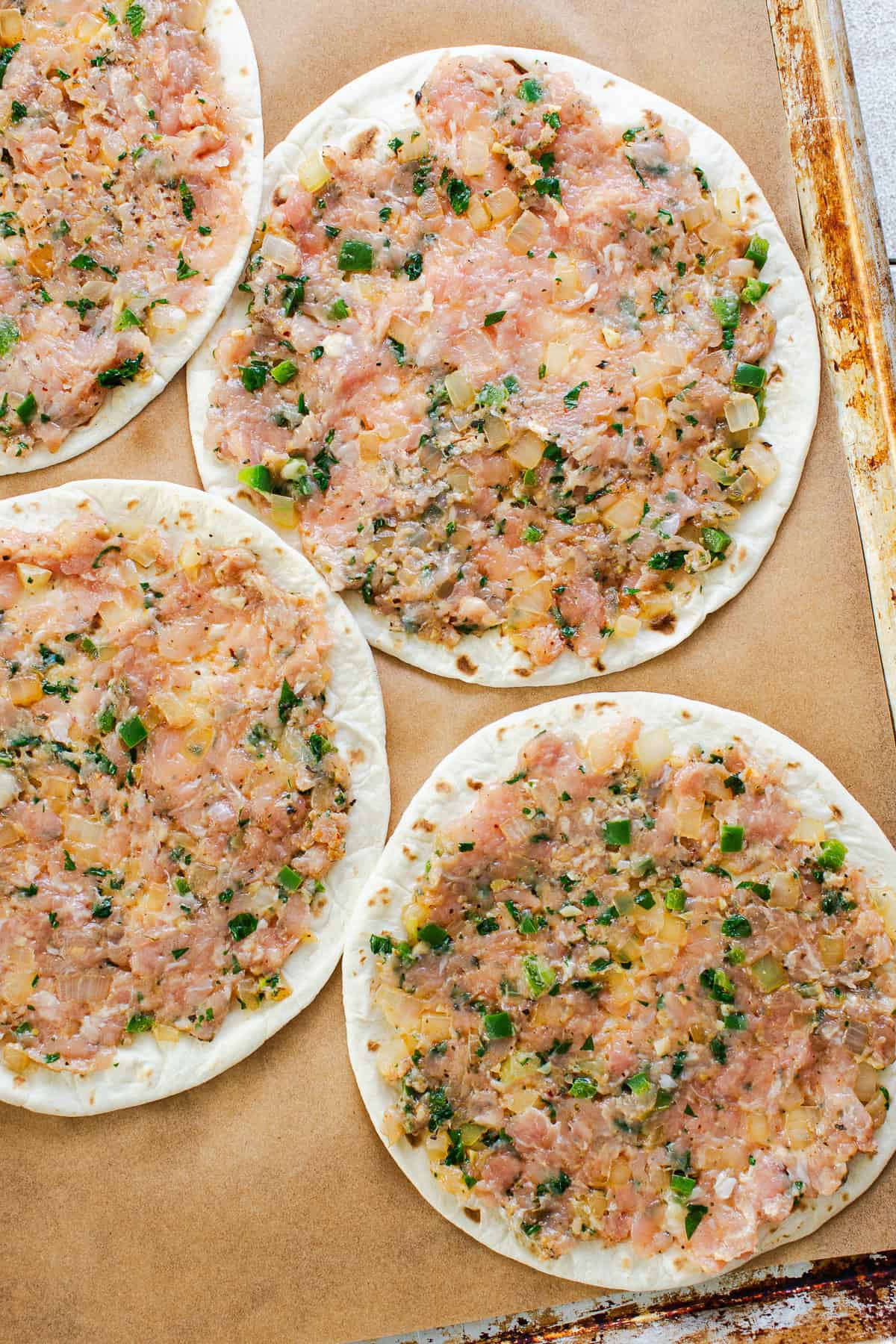 Chicken smash taco mixture spread thin on flour tortillas on a baking sheet.