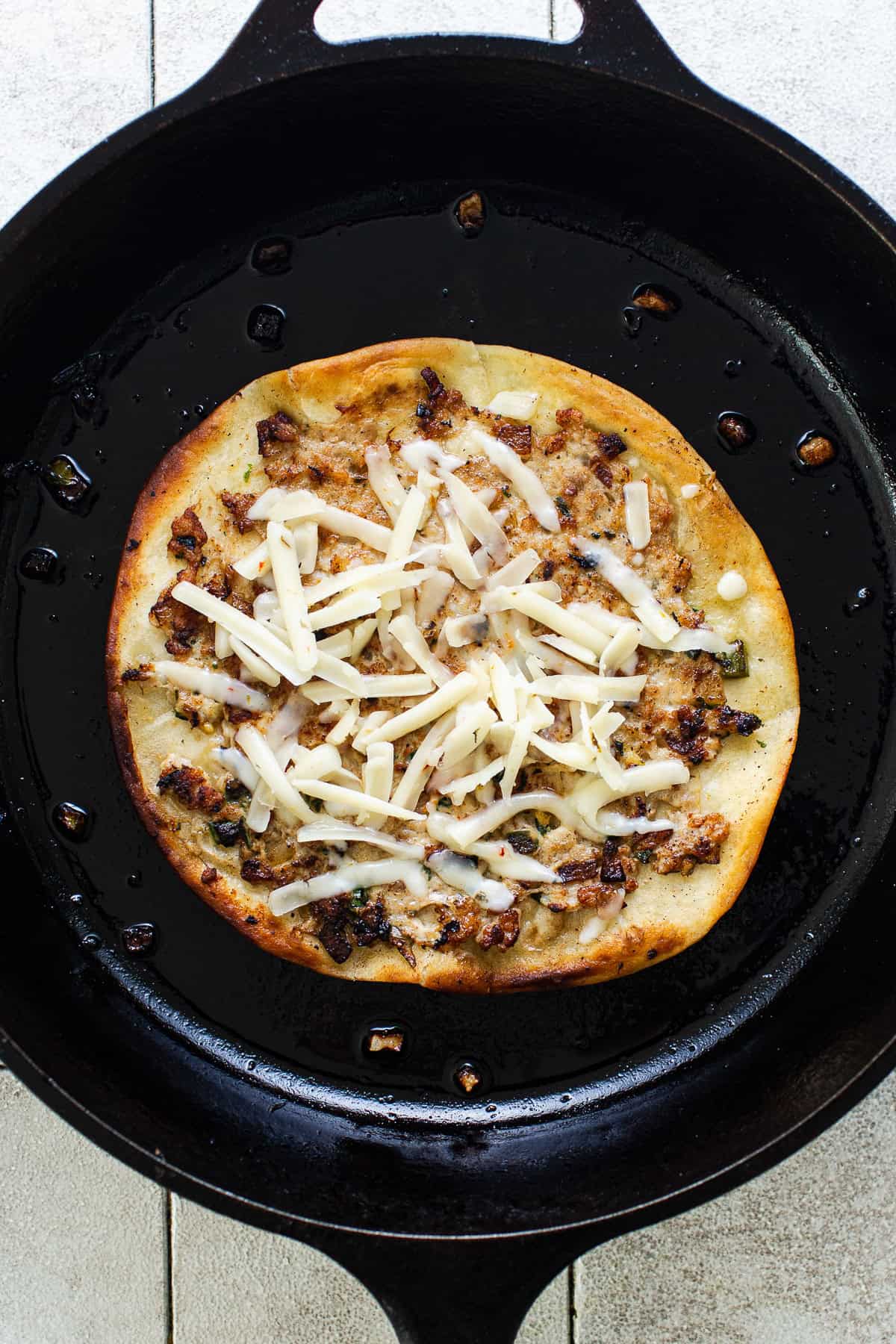 Chicken smash taco cooking crispy-side up, sprinkled with pepper jack before it melts.