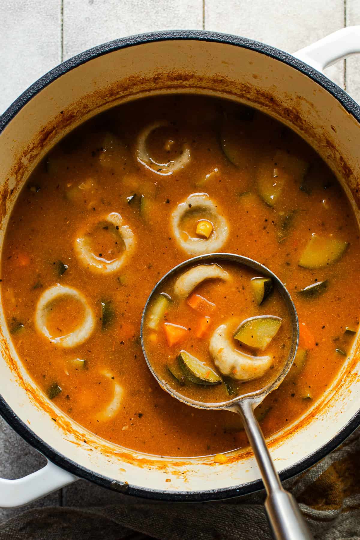 Chochoyotes in a vegetable soup being ladled out of a large pot.