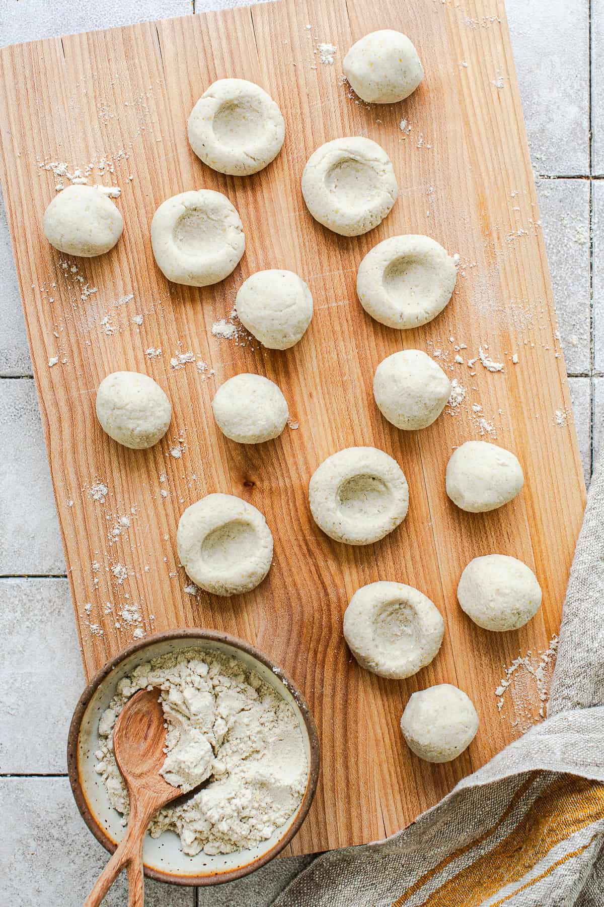 "Chochoyotes being shaped, showing masa dough in a bowl alongside rolled balls and some with the center indentation pressed in"
