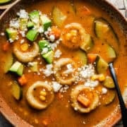 Bowl of chochoyotes in a vegetable soup topped with crumbled queso fresco and diced avocado.