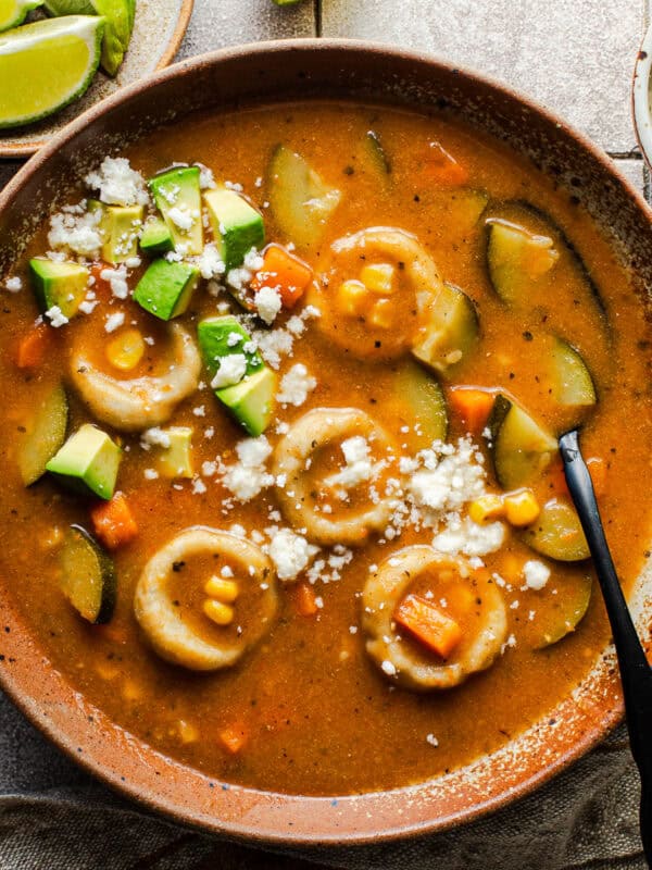 Bowl of chochoyotes in a vegetable soup topped with crumbled queso fresco and diced avocado.