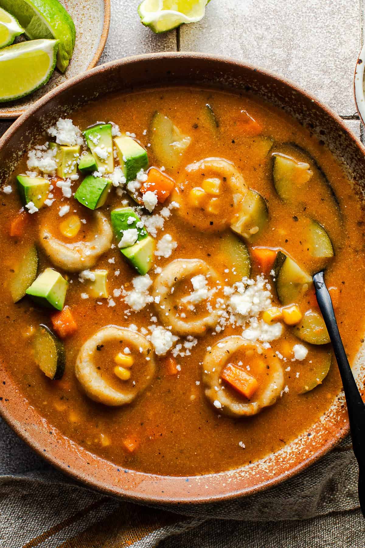 Bowl of chochoyotes in a vegetable soup topped with crumbled queso fresco and diced avocado.