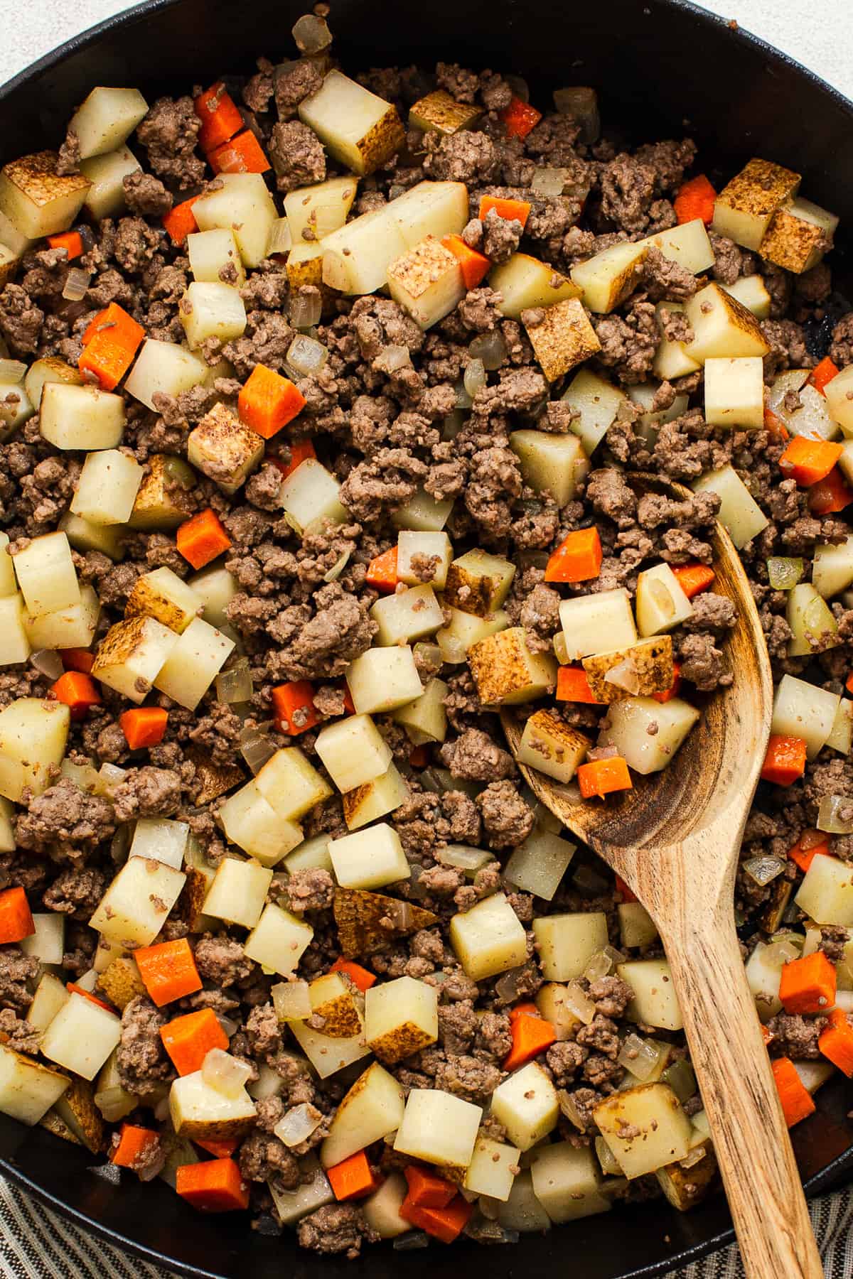 Ground beef, potatoes, and carrots cooking in a skillet for picadillo.