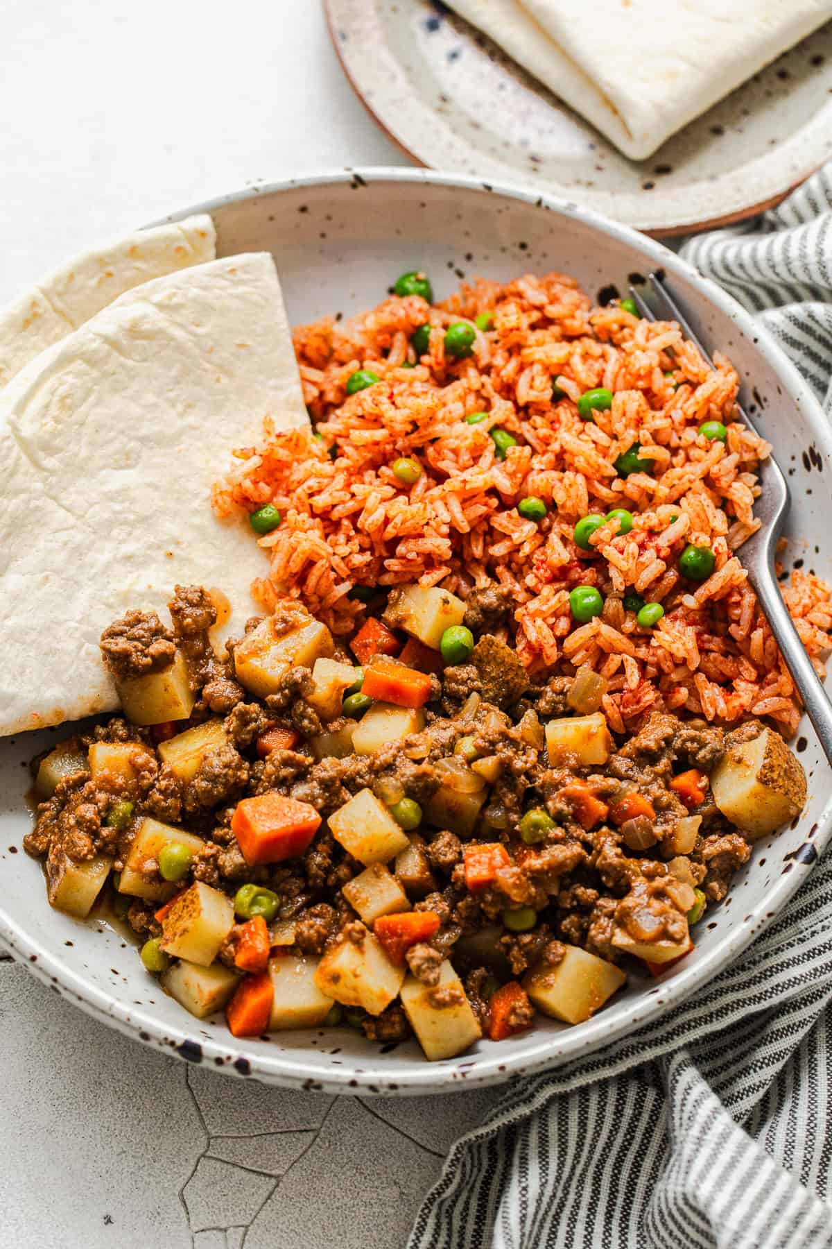 Finished picadillo recipe in a bowl with Mexican rice and served with a flour tortilla on the side.