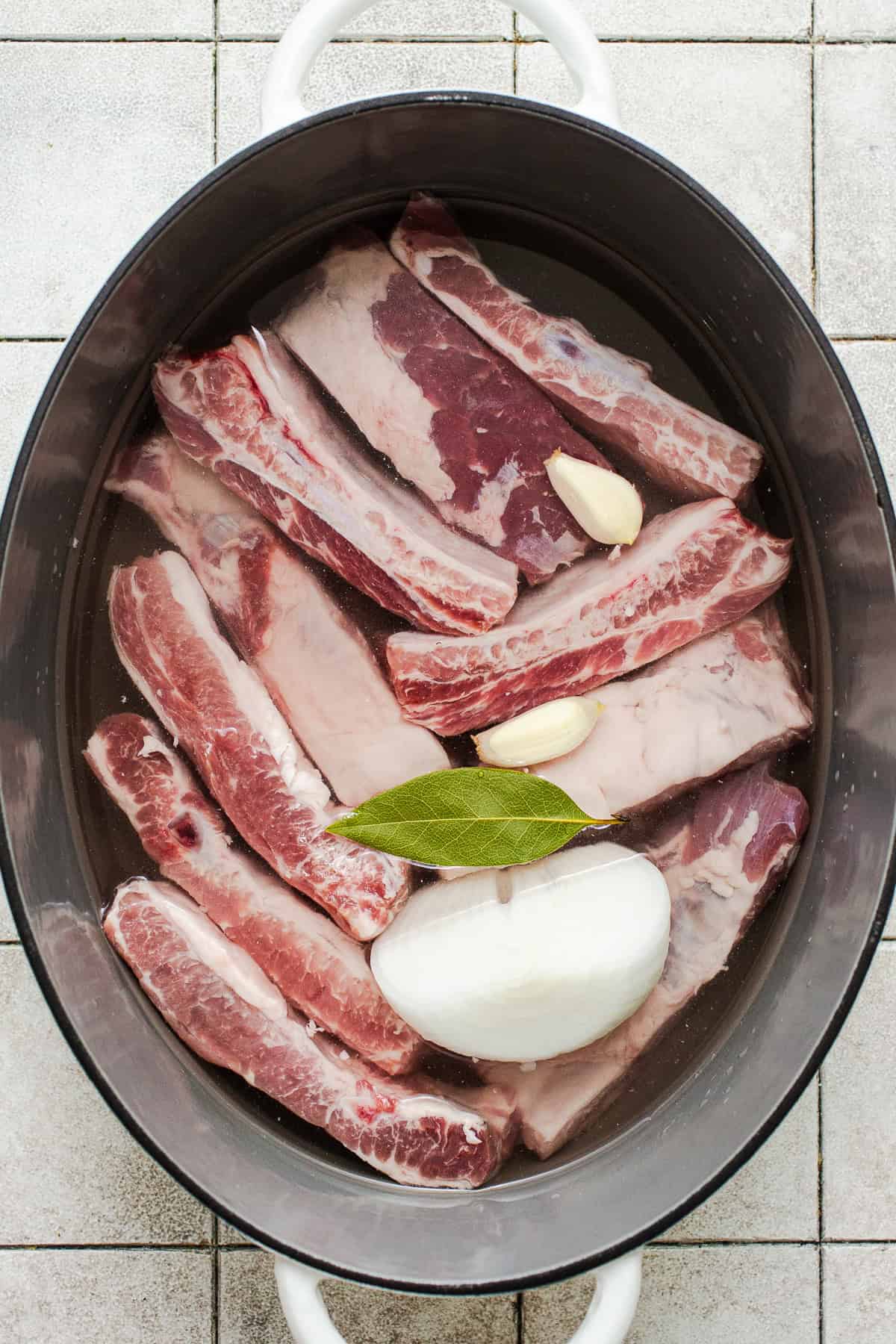Pork ribs in a pot with onion, garlic, and a bay leaf.