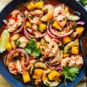 Aguachile rojo in a bowl with cucumber, mango, and red onion served with tostadas.
