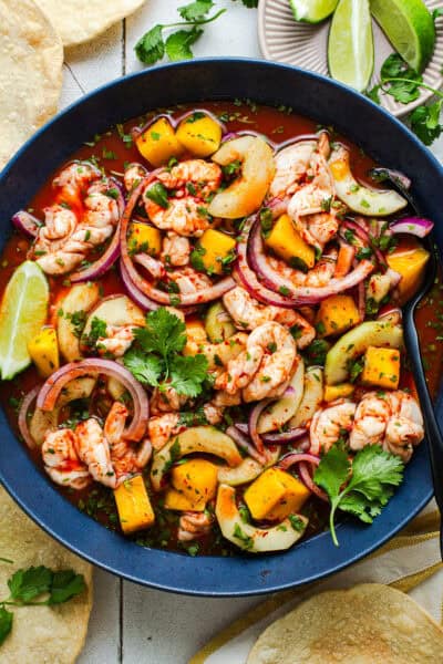Aguachile rojo in a bowl with cucumber, mango, and red onion served with tostadas.