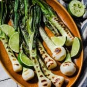 Cebollitas asadas on a platter with lime wedges and Jugo Maggi on the side.
