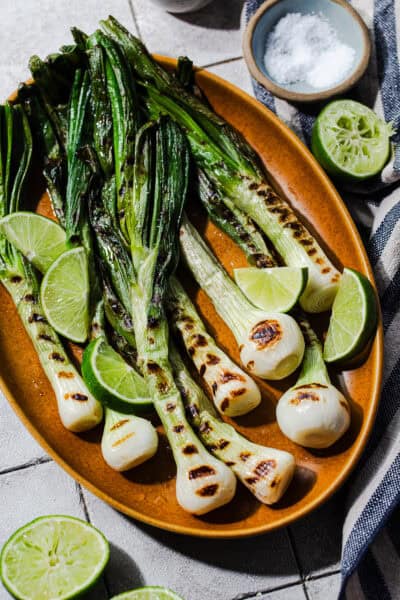 Cebollitas asadas on a platter with lime wedges and Jugo Maggi on the side.