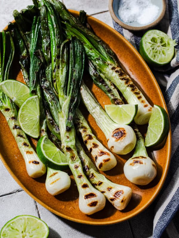 Cebollitas asadas on a platter with lime wedges and Jugo Maggi on the side.
