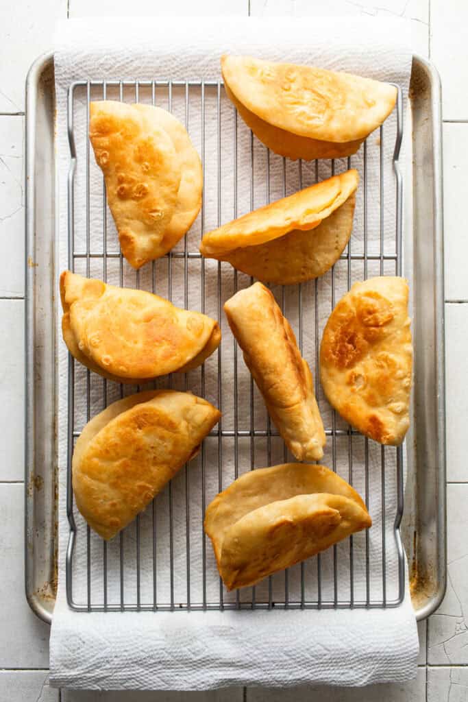 Golden brown fried chalupa shells draining on a paper towel-lined baking sheet.