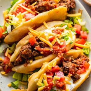 Assembled chalupas topped with ground beef, cheese, lettuce, tomatoes, and sour cream.
