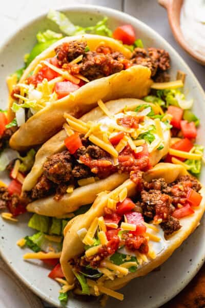 Assembled chalupas topped with ground beef, cheese, lettuce, tomatoes, and sour cream.