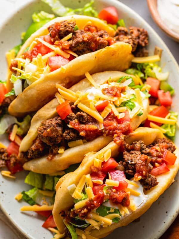 Assembled chalupas topped with ground beef, cheese, lettuce, tomatoes, and sour cream.