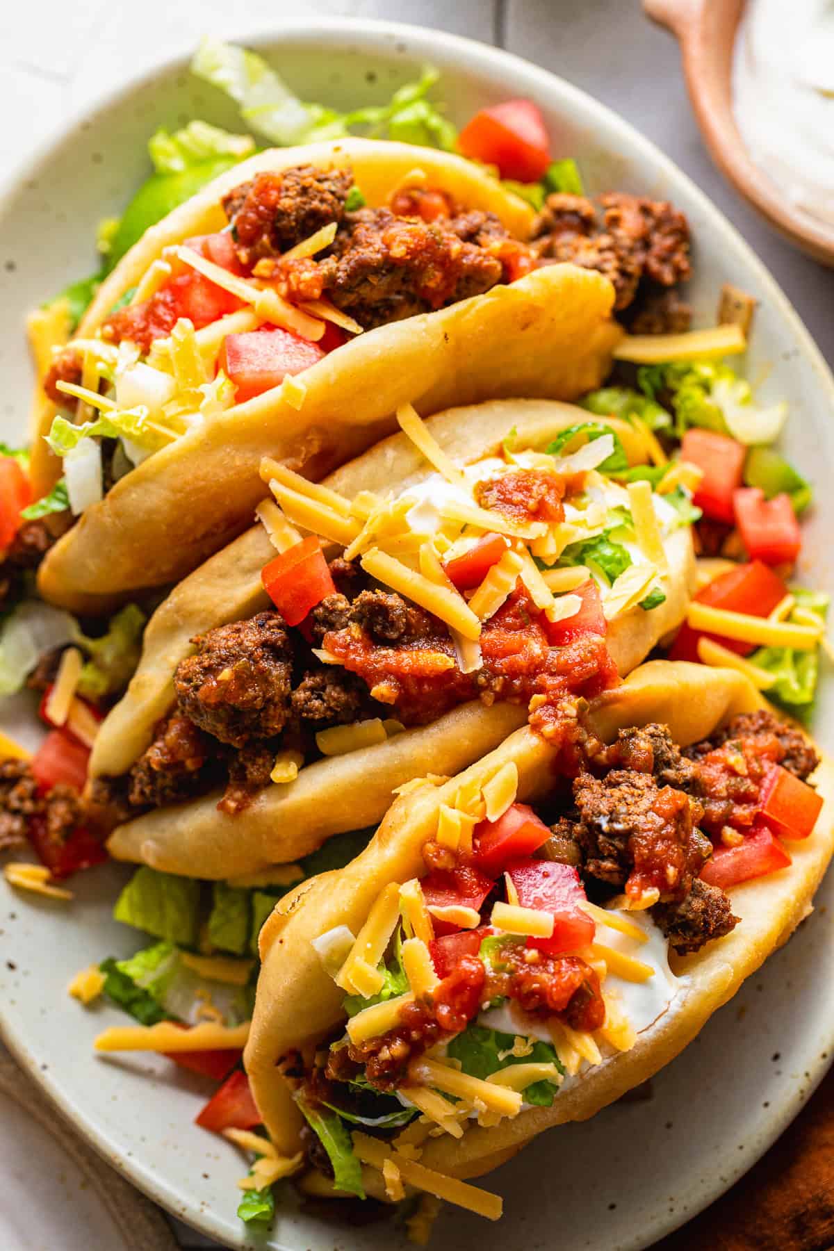 Assembled chalupas topped with ground beef, cheese, lettuce, tomatoes, and sour cream.