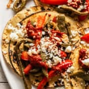 Nopales tacos on corn tortillas topped with queso fresco, guajillo salsa, and peppers and onions.