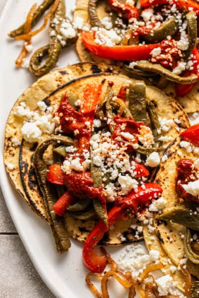 Nopales tacos on corn tortillas topped with queso fresco, guajillo salsa, and peppers and onions.