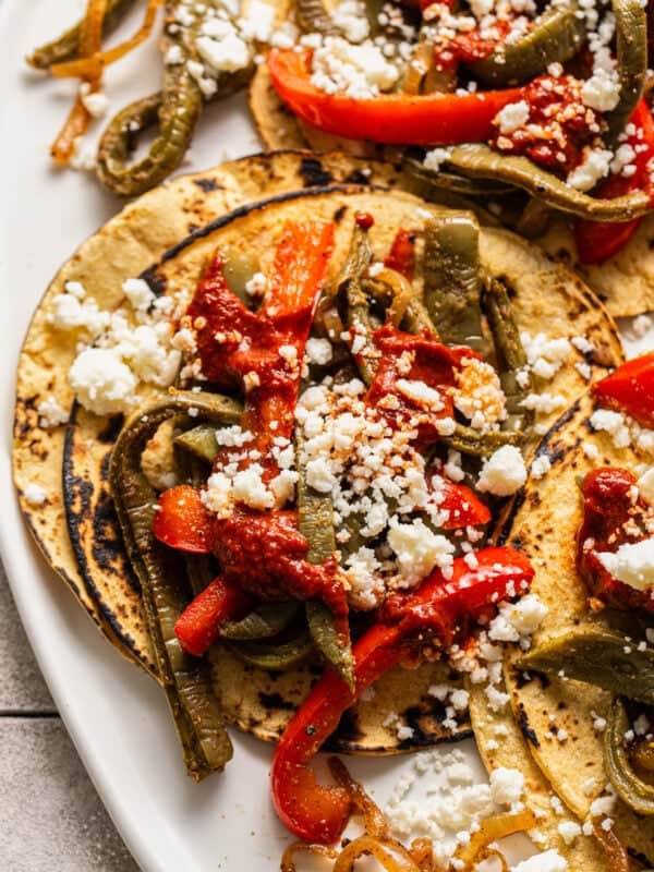 Nopales tacos on corn tortillas topped with queso fresco, guajillo salsa, and peppers and onions.