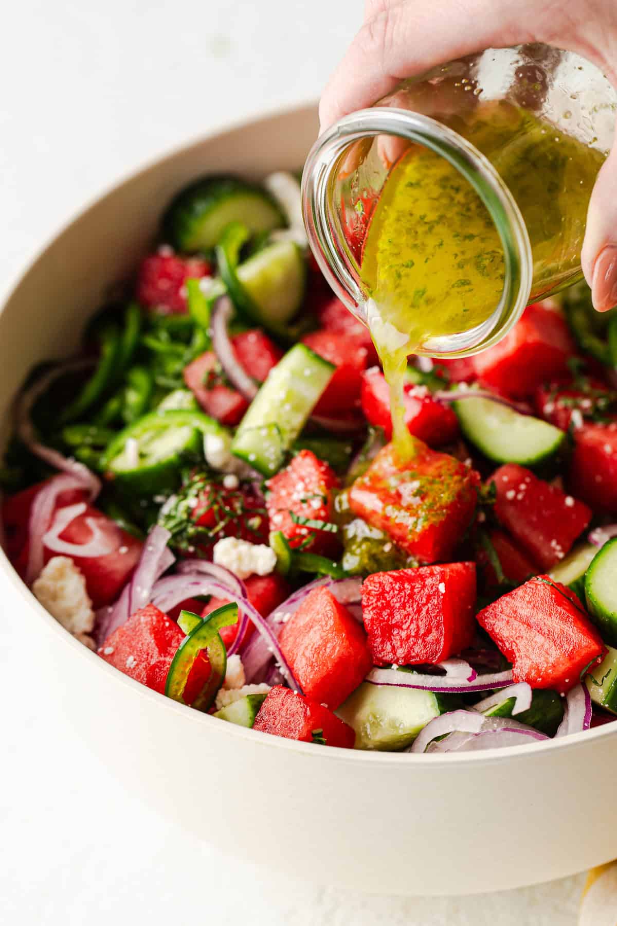 Lime dressing being poured over a bowl of watermelon salad.