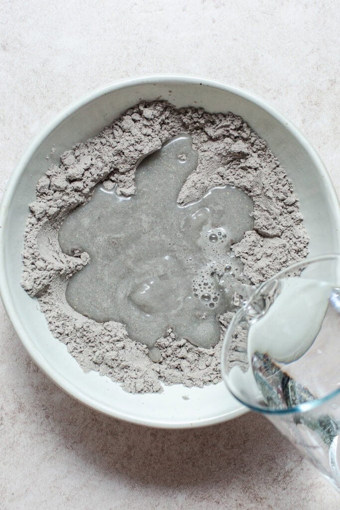 Water being poured into a bowl of blue corn masa for making blue corn tortillas.