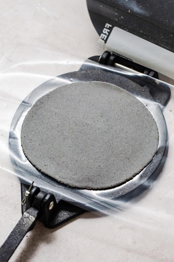 A blue corn tortilla pressed flat on a tortilla press.