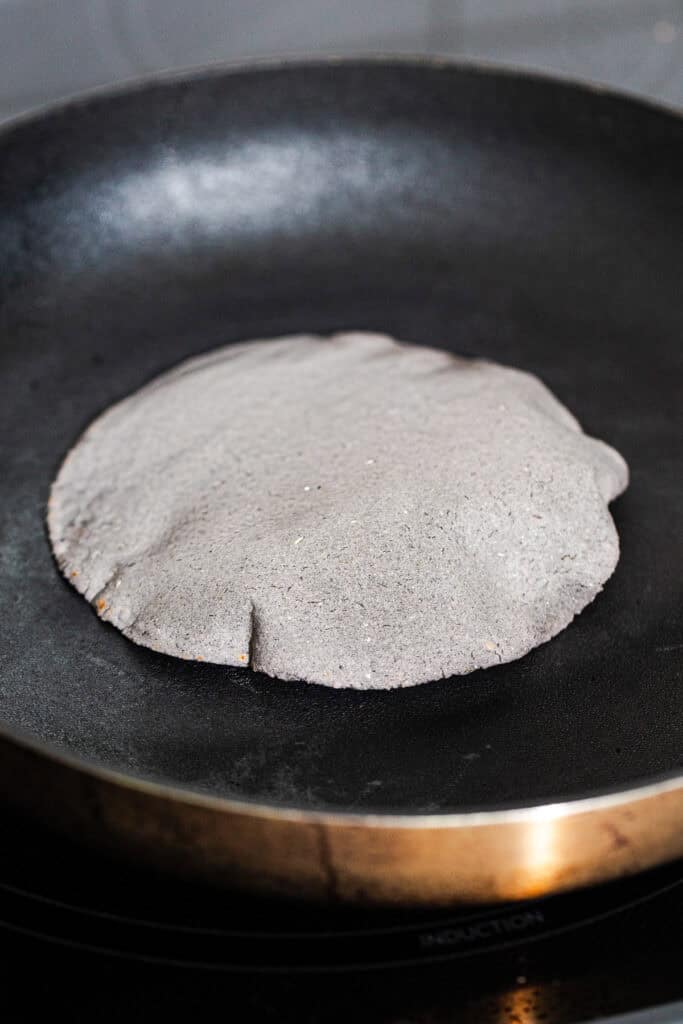 A blue corn tortilla cooking and puffing on a hot skillet.
