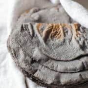 Blue corn tortillas on a white kitchen towel ready to be eaten.