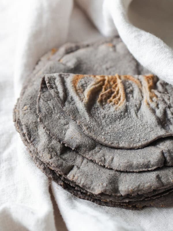 Blue corn tortillas on a white kitchen towel ready to be eaten.