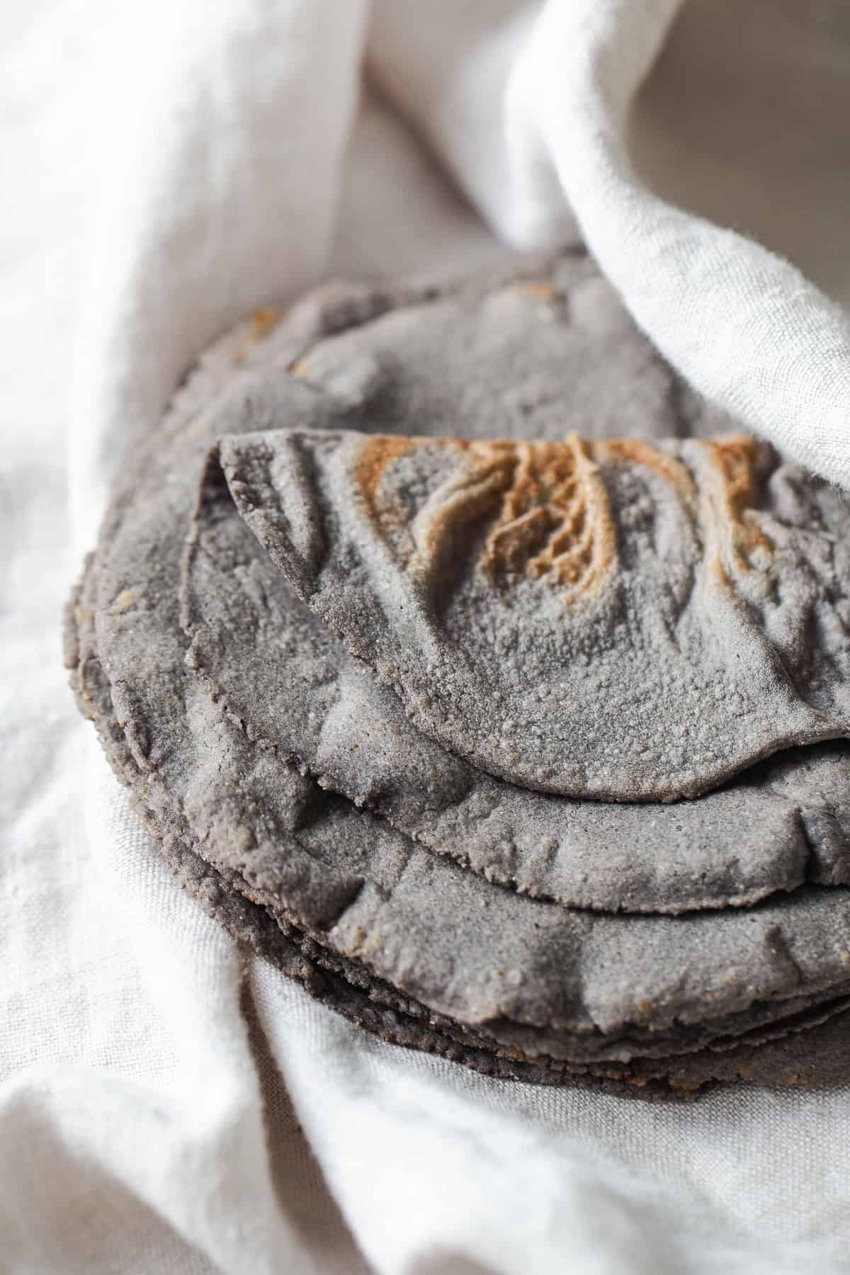 Blue corn tortillas on a white kitchen towel ready to be eaten.