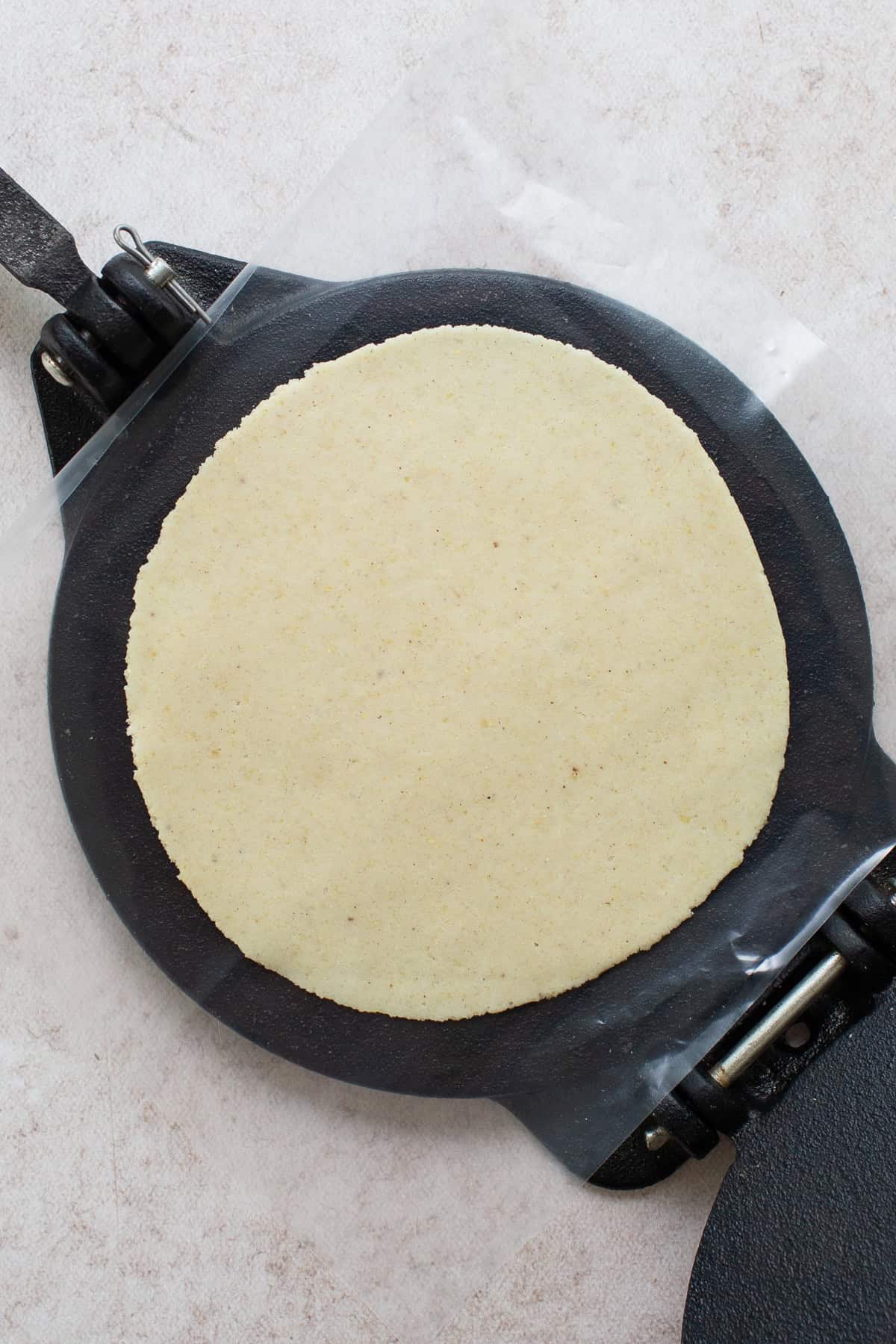 Corn tortilla dough pressed flat on a tortilla press lined with plastic.