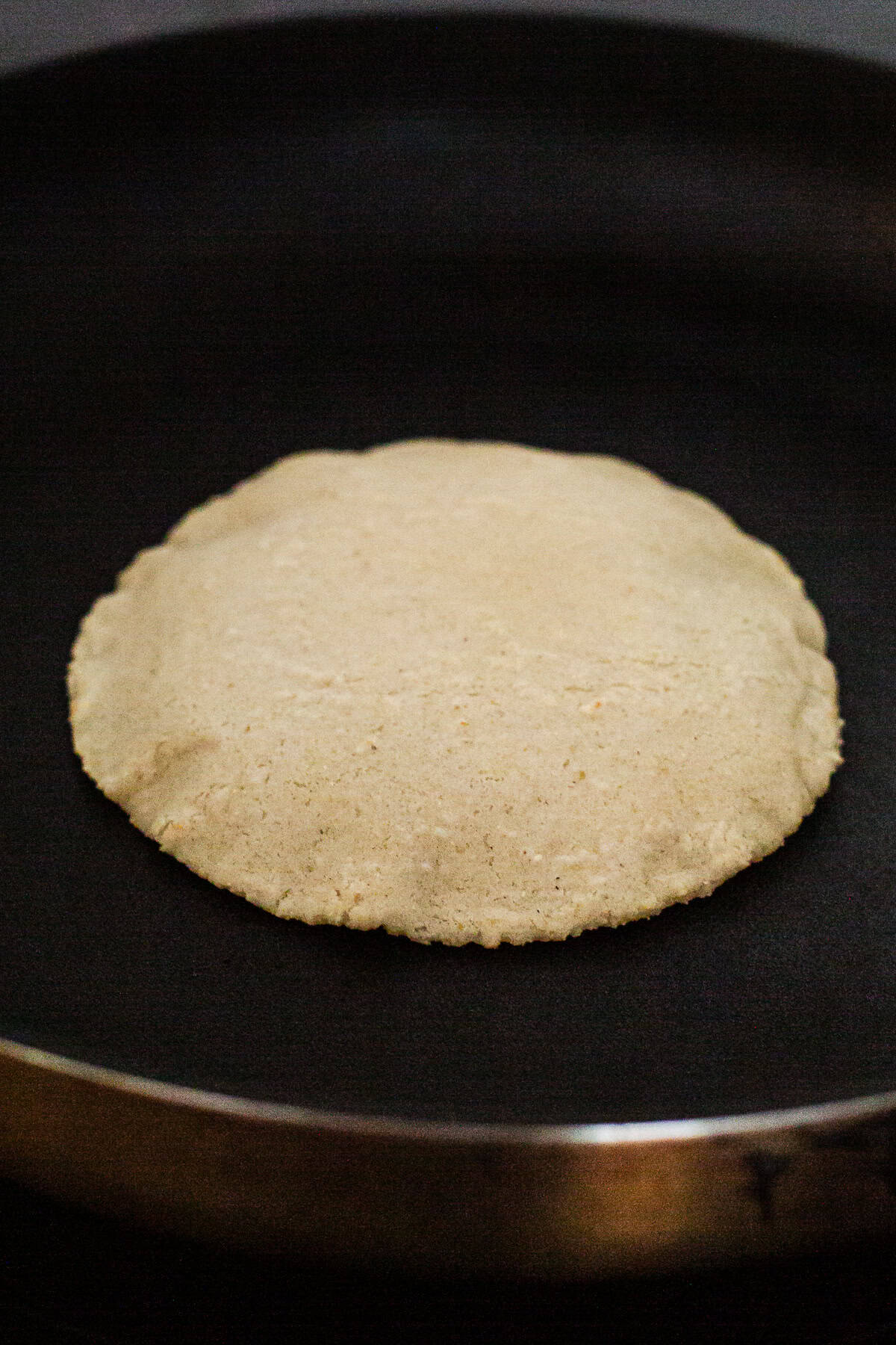 Corn tortilla puffing up in a hot nonstick skillet.
