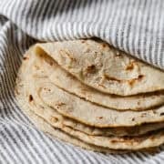 Stack of homemade corn tortillas on a kitchen towel with one folded over.