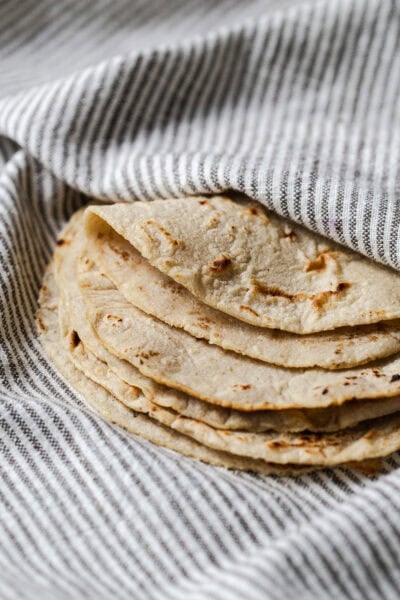 Stack of homemade corn tortillas on a kitchen towel with one folded over.