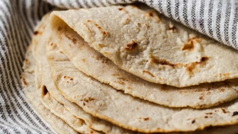 Stack of homemade corn tortillas on a kitchen towel with one folded over.