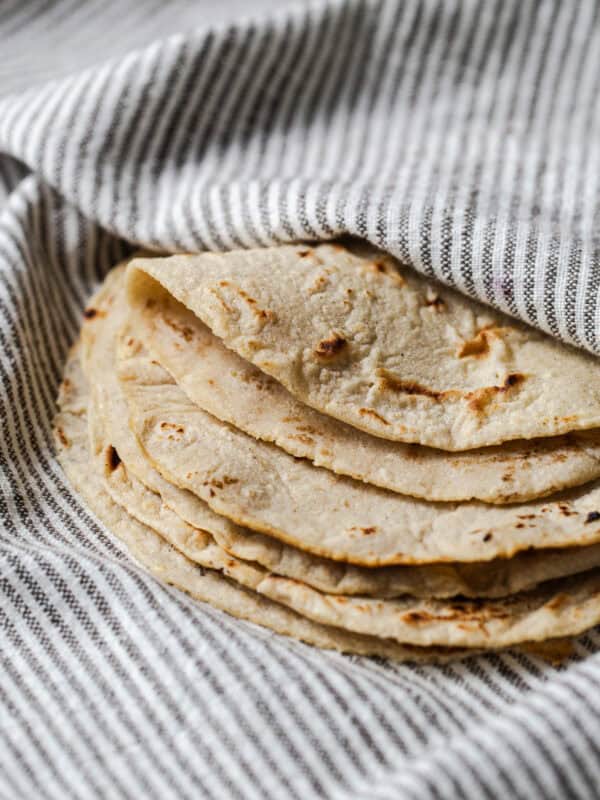 Stack of homemade corn tortillas on a kitchen towel with one folded over.
