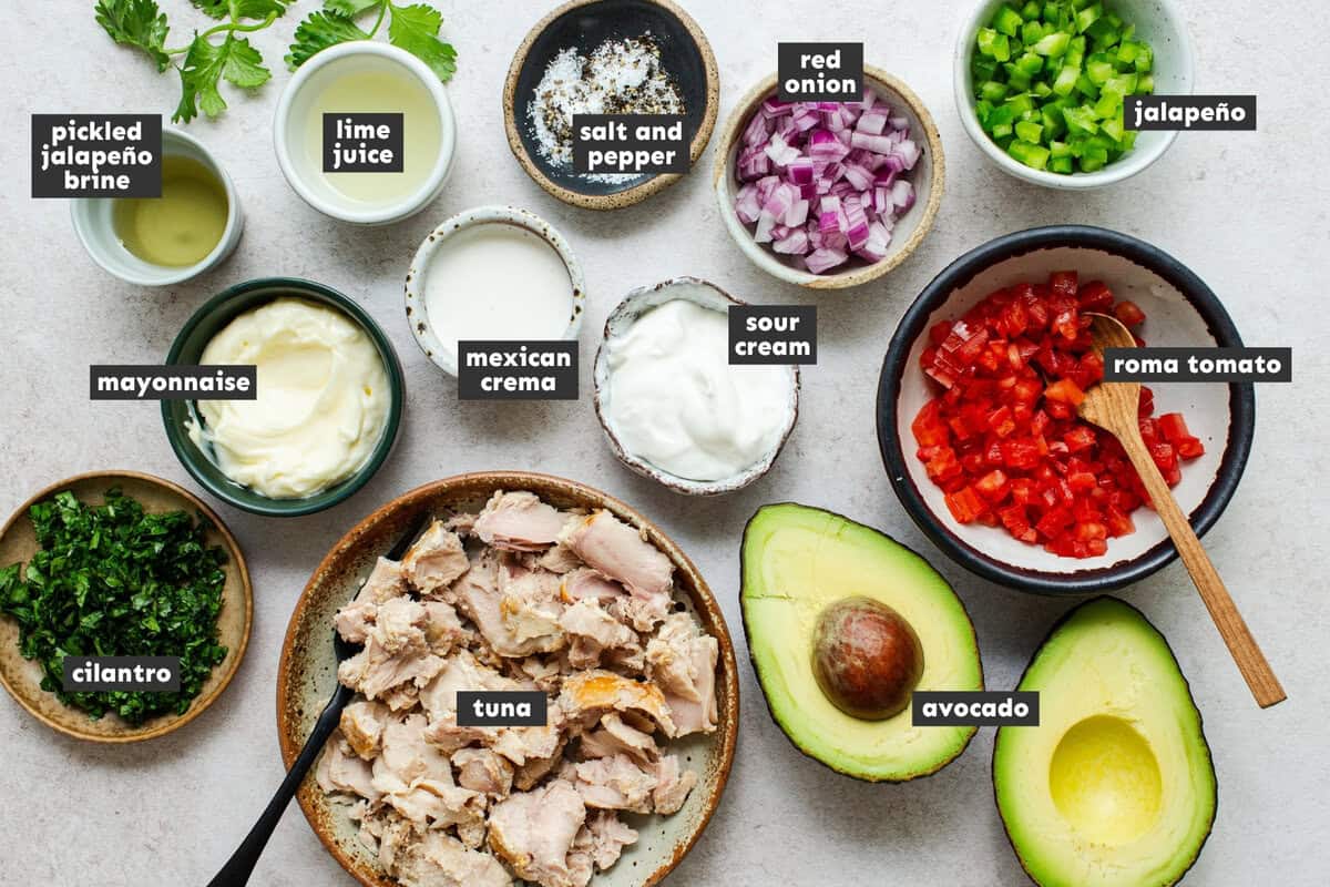 Ingredients for Mexican tuna salad including canned tuna, Roma tomato, jalapeño, red onion, cilantro, avocado, and Mexican crema.
