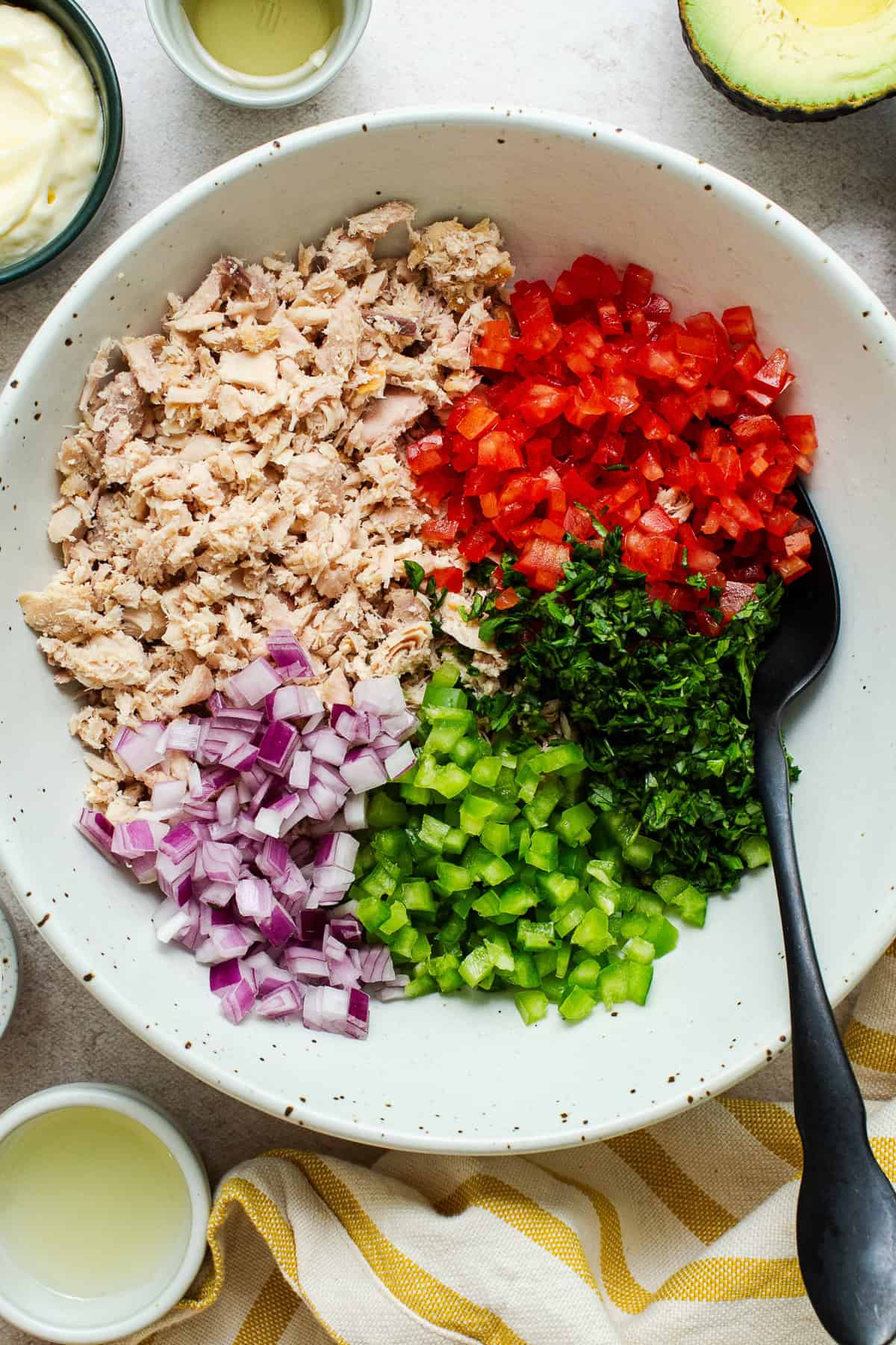 Flaked tuna, diced tomato, jalapeño, red onion, and cilantro arranged in sections in a large bowl for Mexican tuna salad.