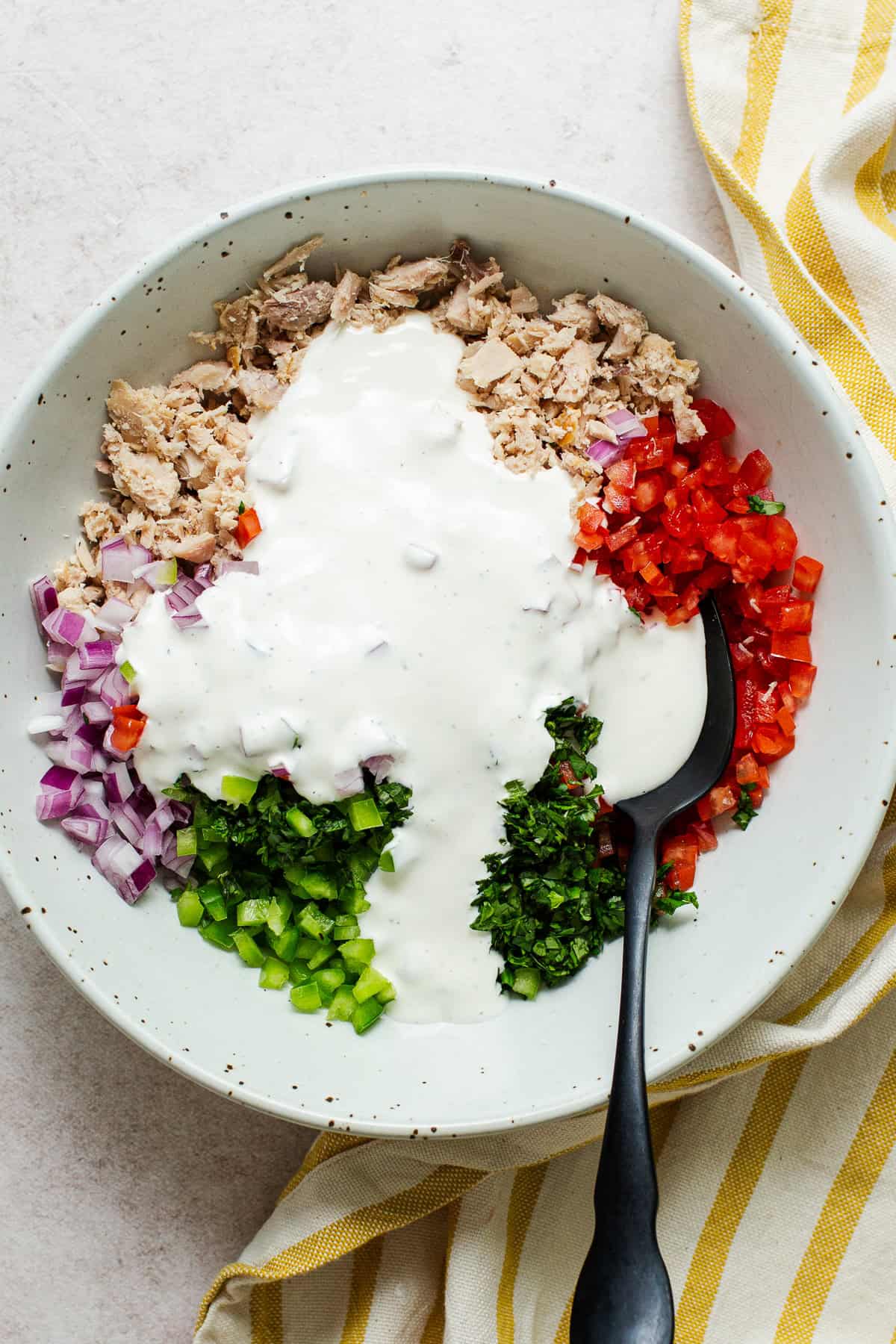 Creamy dressing poured over the tuna and vegetables in a bowl before mixing the Mexican tuna salad together.