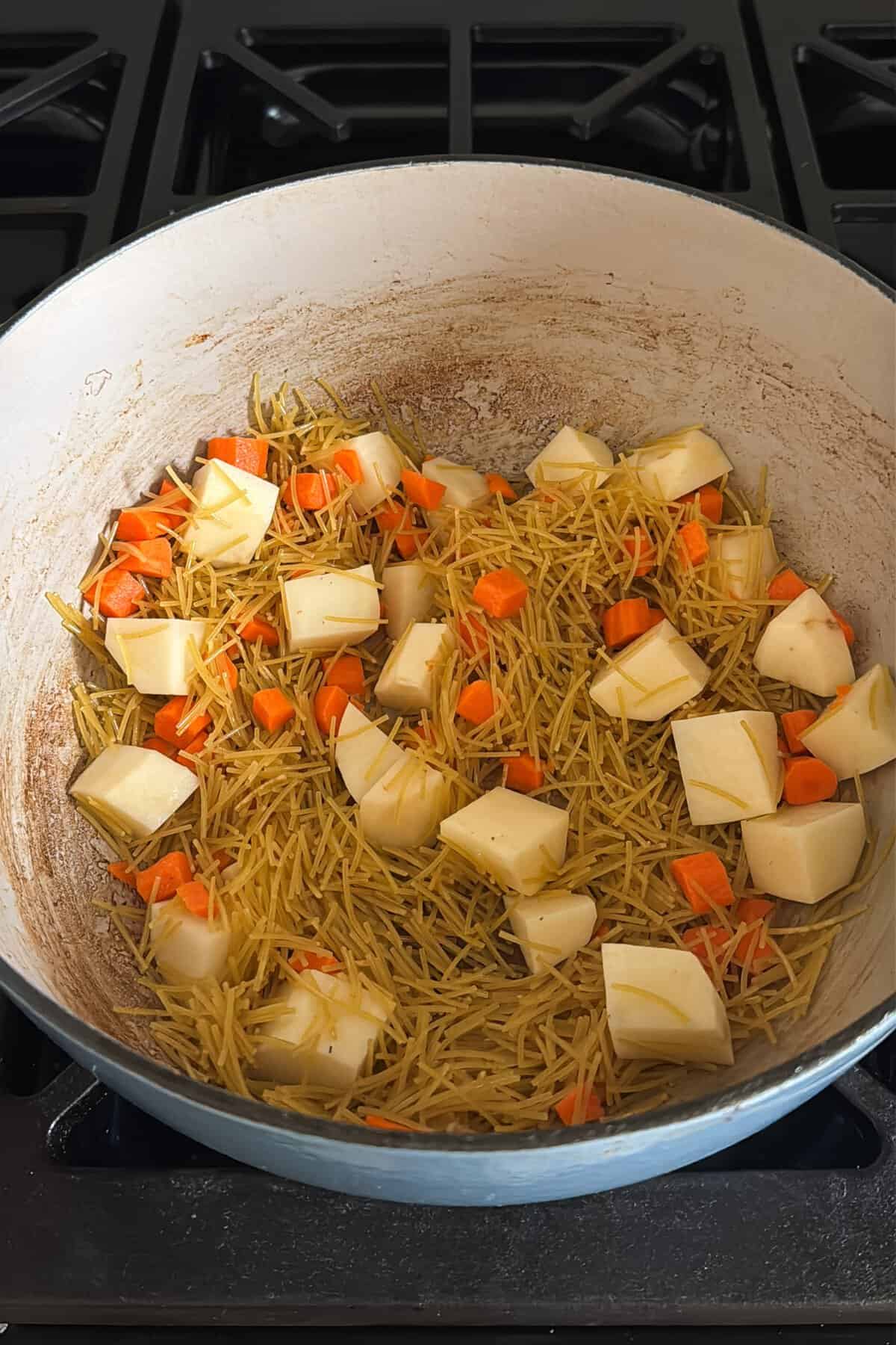 Toasted fideo noodles, carrots, and potatoes in a large Dutch oven.