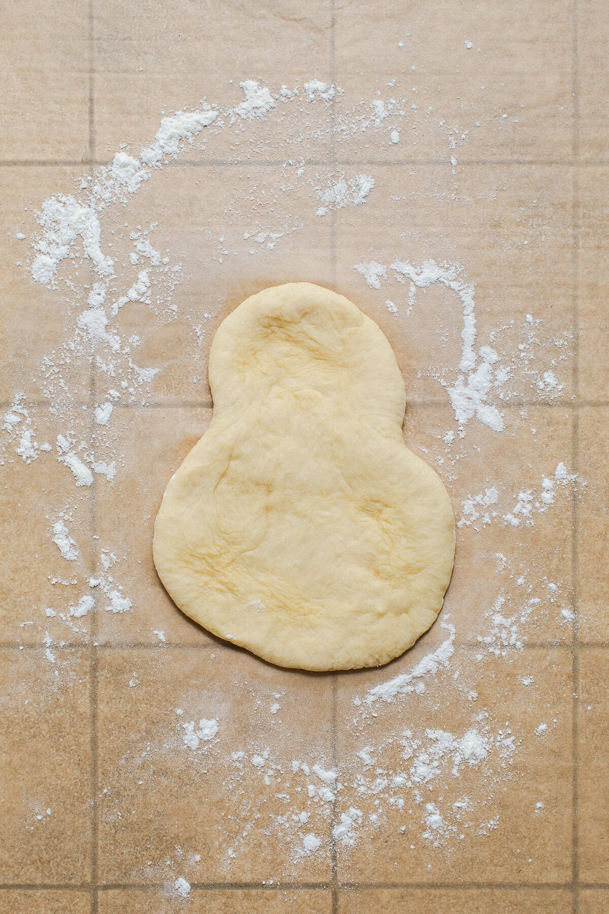 Cemita bun dough flattened into a snowman shape on a floured surface.