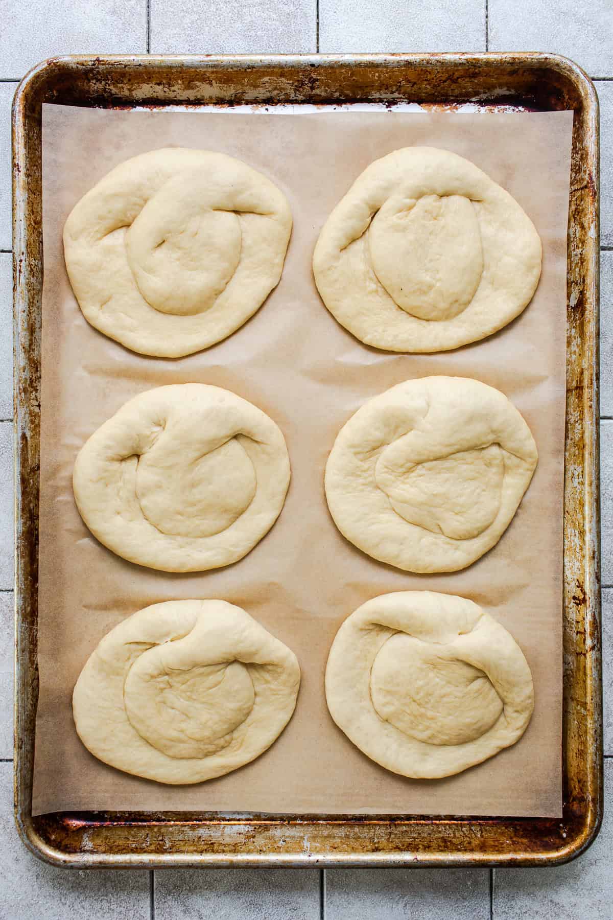 Six shaped cemita buns on a parchment-lined baking sheet before rising.