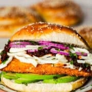 A cemita poblana sandwich with crispy chicken milanesa, avocado, and stringy quesillo or Oaxaca cheese on a sesame bun.