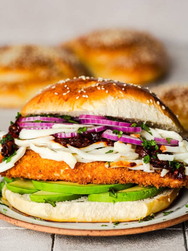 A cemita poblana sandwich with crispy chicken milanesa, avocado, and stringy quesillo or Oaxaca cheese on a sesame bun.