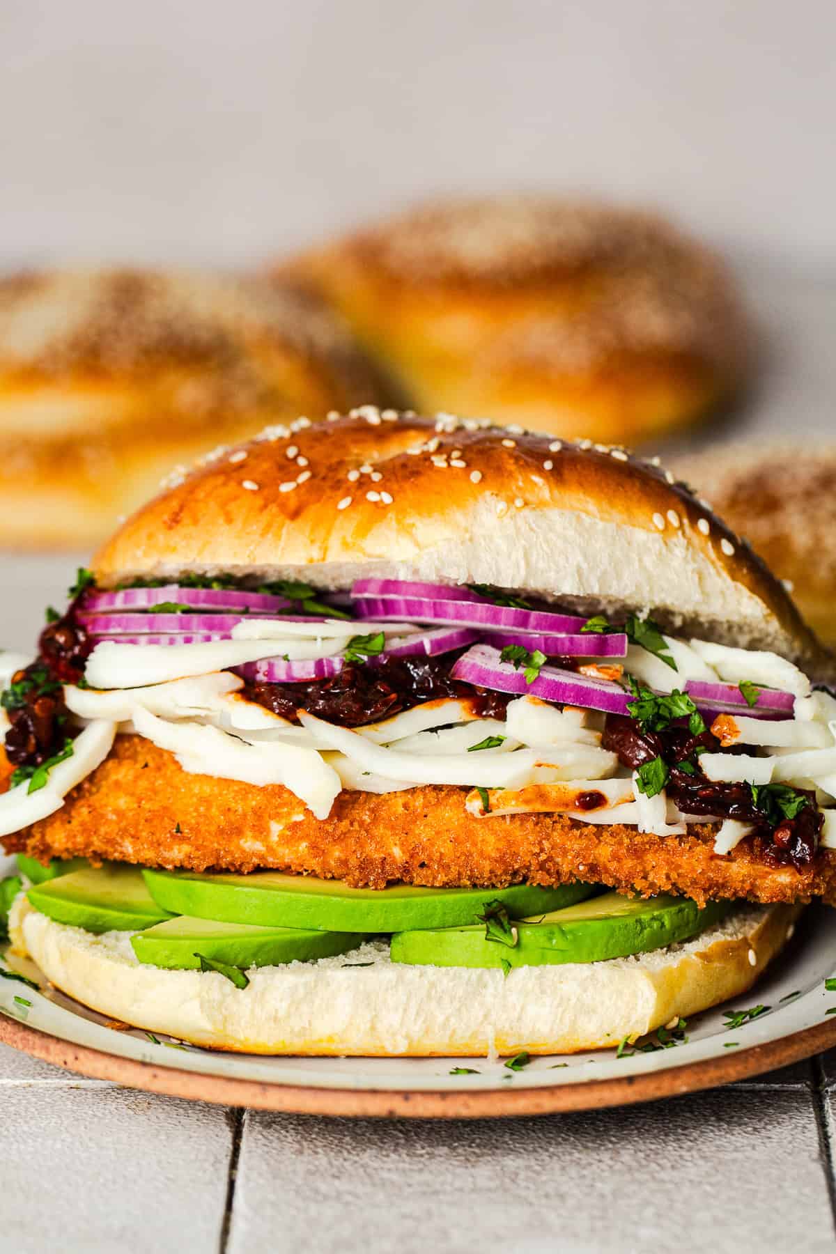 A cemita poblana sandwich with crispy chicken milanesa, avocado, and stringy quesillo or Oaxaca cheese on a sesame bun.