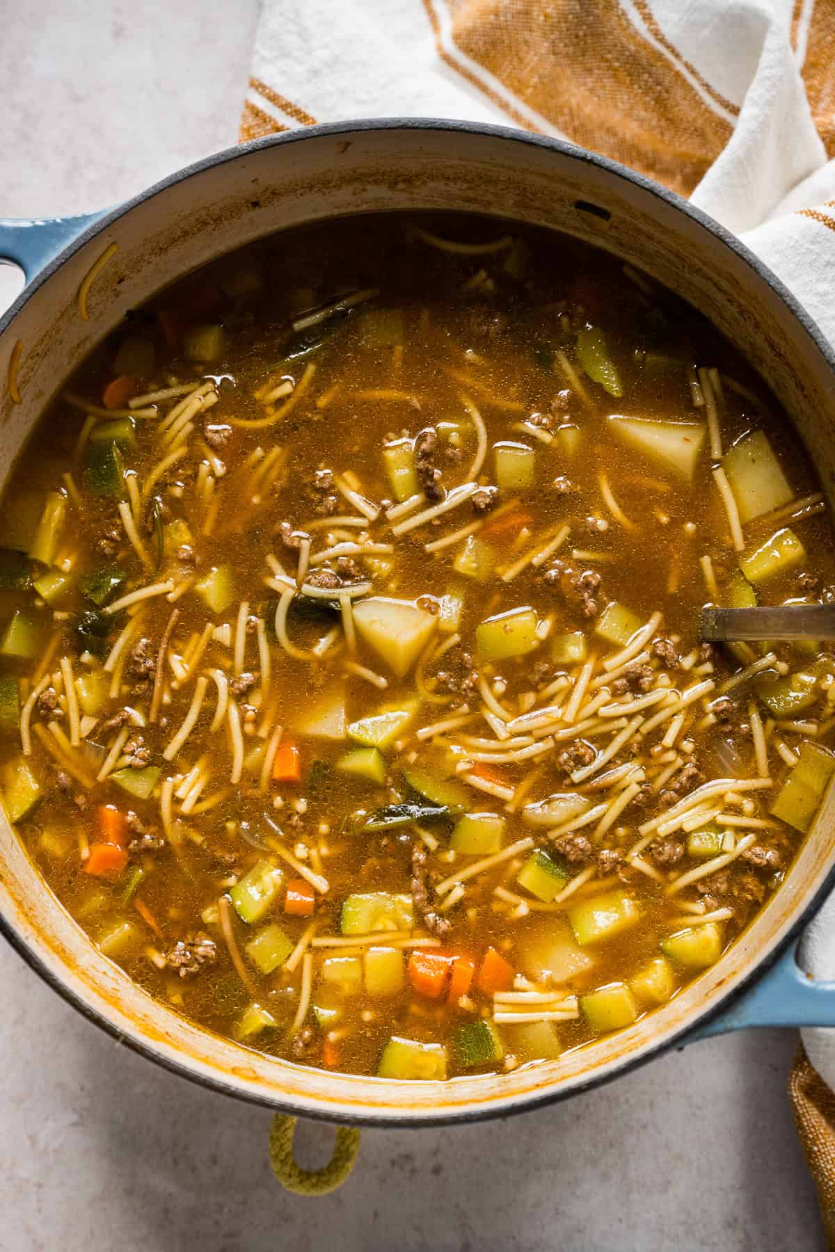 A large pot filled with sopa de fideo con carne molida with potatoes, carrots, and zucchini ready to be eaten.