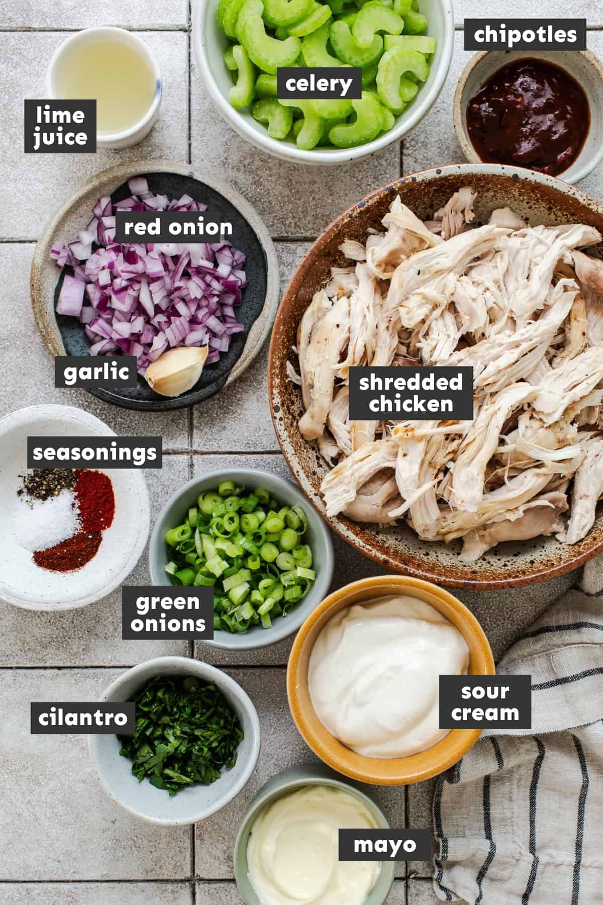 Ingredients for chipotle chicken salad, including shredded chicken, celery, red onion, cilantro, green onion, mayo, sour cream, and chipotles in adobo.